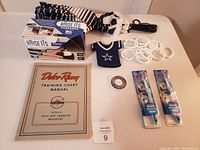 Photo showing all lot items on table including Delsco Remy manual, Frozen toothbrushes, Raise Its beer holder box, pet accessories, beverage koozie, and round token.