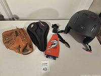 Photo of four sports-related items: Wilson baseball catcher's mitt, padded bike seat with cover, skateboard helmet size medium, and NFL beer holder.