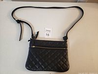 Front view of the black quilted purse showing the adjustable crossbody strap and gold-tone zipper pocket.