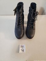 Front view of black women's ankle boots with laces on gold-tone eyelets and rounded toes.