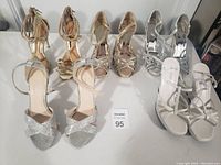 Four pairs of women's sparkly dress shoes in silver and gold tones, two with glitter and two metallic, arranged in a row on a white surface.