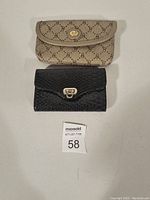 Two women's wallets placed flat: one beige with repeating GG monogram and gold lock, the other black textured leather with silver lock.
