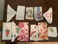View of 11 assorted handkerchiefs laid out on table, showing various embroidered and printed floral designs and holiday motifs.