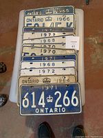 Photo showing the full lot of 12 vintage Ontario license plates stacked in a pile with visible year markings.