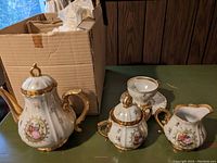 Porcelain tea set pieces displayed out of original packaging, including tea pot, cream pitcher, sugar bowl, and partial view of tea cups.