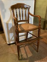 Front view of antique toddler chair showing wooden spindled backrest and caned seat.