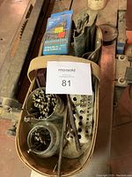 Quart basket filled with various wood drill bits, some loose in jars and some in a leather pouch. Includes a metal perforated holder and various sized drill bits.