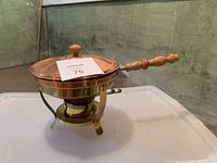Side view of the copper chafing dish on its metal stand showing wooden handle and lid with wooden knob.