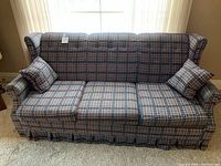 Front view of the sofa couch with plaid upholstery, skirted bottom and 2 matching pillows