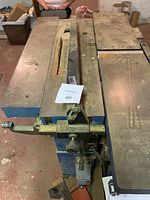 Photo showing table saw station with visible blade, fence, and adjustment handles, displaying heavy use and dust accumulation.