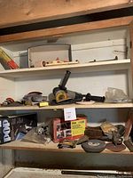 Photo showing three shelves with various power tools and hand tools including Black and Decker pop rivet tool kit, electric stapler, sanding discs, planer, and more, all used.