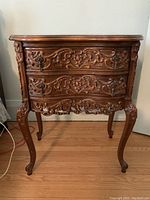 Front view showing two carved drawers with ornate handles and detailed carving on legs and frame.