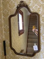 Front view of the mirror showing curved frame, decorative crest at the top, and reflection of surrounding interior.