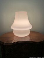 Lit glass table lamp showing smooth curved form and soft glow on wooden surface.