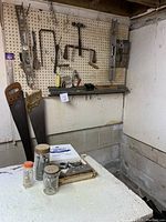 Photo of a pegboard mounted with various hand tools including hand saws, coping saw, levels, clamps. Also includes three jars and toolboxes on a table below.