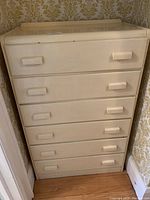 Front view of the dresser showing all six drawers and rectangular wood handles, painted cream/off-white with visible wear and dings.