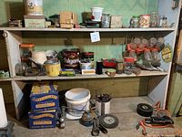 Shelf with multiple jars and boxes containing assorted hardware fasteners such as nails, screws, and bolts, with some tools and tape visible.