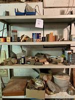 Four metal shelves with assorted fasteners, screws, nuts, bolts, blades, and other hardware items placed loosely and in containers.