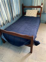 Full view of the twin bed frame with a navy blue comforter and floral pillow, showing the footboard and parts of adjacent curtains and wall.