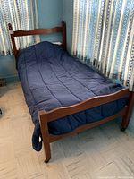 Full view of twin size wooden bed frame with navy bedding, positioned in corner near patterned curtains