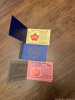 Photo of two vintage Famous Players coupons on a wooden floor. One is a yellow $1 ticket with a red maple leaf logo, and the other is a pink bonus ticket. Both have fold-out informational inserts in blue and black text attached.