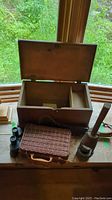 Photo showing open wooden box with interior compartments, small wicker basket, wooden churn tool, binoculars nearby