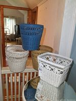 Four wicker baskets in blue, white, and natural colors positioned on a beige surface in a room with wooden paneled walls.