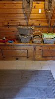 Photo of assorted handled wicker baskets with two large rectangular wicker baskets stacked, a smaller round wicker basket, small garden tools, dustpan and brooms in background.