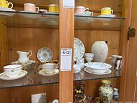Cabinet with mixed china items including cups, plates, bowls, vases, and figurines