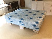Side angle photo of the mattress and boxspring set on wooden blocks, showing the blue and white floral patterned upholstery.