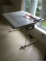 Full view of the drafting table at an angle showing the light-up glass top and rulers placed on surface.