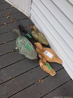 Photo showing four wooden duck decoys arranged on floor against wall: various sizes, two with greenish gray paint, one painted brownish tone, one natural wood. All show wear, some paint loss.