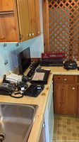 Kitchen countertop with RCA 24-inch LED HDTV screen, Samsung sound bar, Mitsubishi VCR unit, cords and remotes.