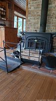 Wide shot showing both cast iron hearths in front of wood stove, Ecofan fan behind, ash bucket to right, pot on stove.
