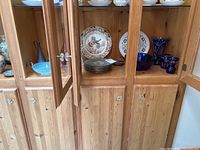 Wooden cabinet display with cobalt blue glass bowl, brown glass vases, decorative plates including Windsor Ware Wild Turkeys, glass bird figurines, pitcher, and additional plates.