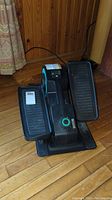 Front view of Cubii mini elliptical showing two large black foot pedals and central flywheel casing with teal accent and power cord.