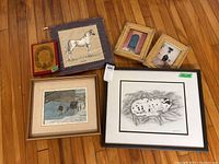 Seven framed artwork pieces arranged on wooden floor: three prints including 'Blue Roofs Cairo' and Peter Snyder drawing, 5x7 Christmas plaque, Arabian horse textile art, and two matching framed prints.