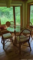 Full view of rattan table with round glass top surrounded by four rattan chairs with cushions.