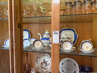 Wide view of cabinet shelf showing entire porcelain tea set including teapot, cups, saucers, and serving plates