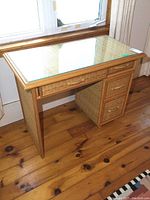 Front and side perspective of the wicker desk showing four drawers and glass top.