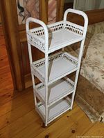 Full view of white wicker shelf on hardwood floor next to floral upholstered couch.