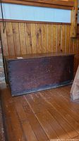 Front view of vintage wooden chest showing lift top, dark worn finish with scratches and crack on the top surface.
