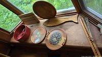 View of the wooden trays with artwork, wooden bowl, wooden salad tongs, cutting boards including fish-shaped board, and round tray on window ledge.