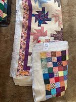 Photo showing two folded unfinished quilts stacked, one with pinwheel design and floral border, the other with small square multi-color patchwork.