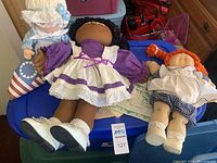 Two Cabbage Patch dolls and one rag doll laid on blue plastic tub, showing one with adoption papers and detailed clothing