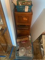 Oak two drawer cupboard filled with assorted craft supplies in bins and boxes, including paper and cartons.