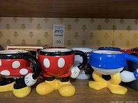 Photo shows novelty-shaped Disney character mugs resembling Mickey Mouse's shorts and Donald Duck's feet, with other traditional style mugs behind them.