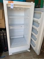 Full view of white Frigidaire commercial upright freezer with door open showing wire shelves and door racks