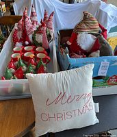 Wide view showing collection of ceramic gnome shakers, red mugs, stuffed gnomes in a box, and throw pillow.