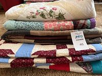 Stacked view of five different folded quilts showing multiple layers with floral and patchwork designs in various colors.